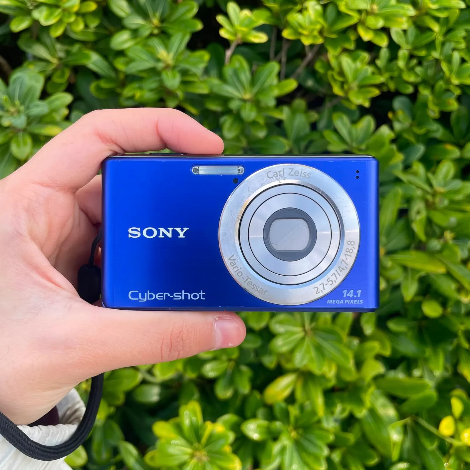 Cámara Sony Cyber-shot azul sostenida en una mano, de frente, con el objetivo Carl Zeiss a la vista