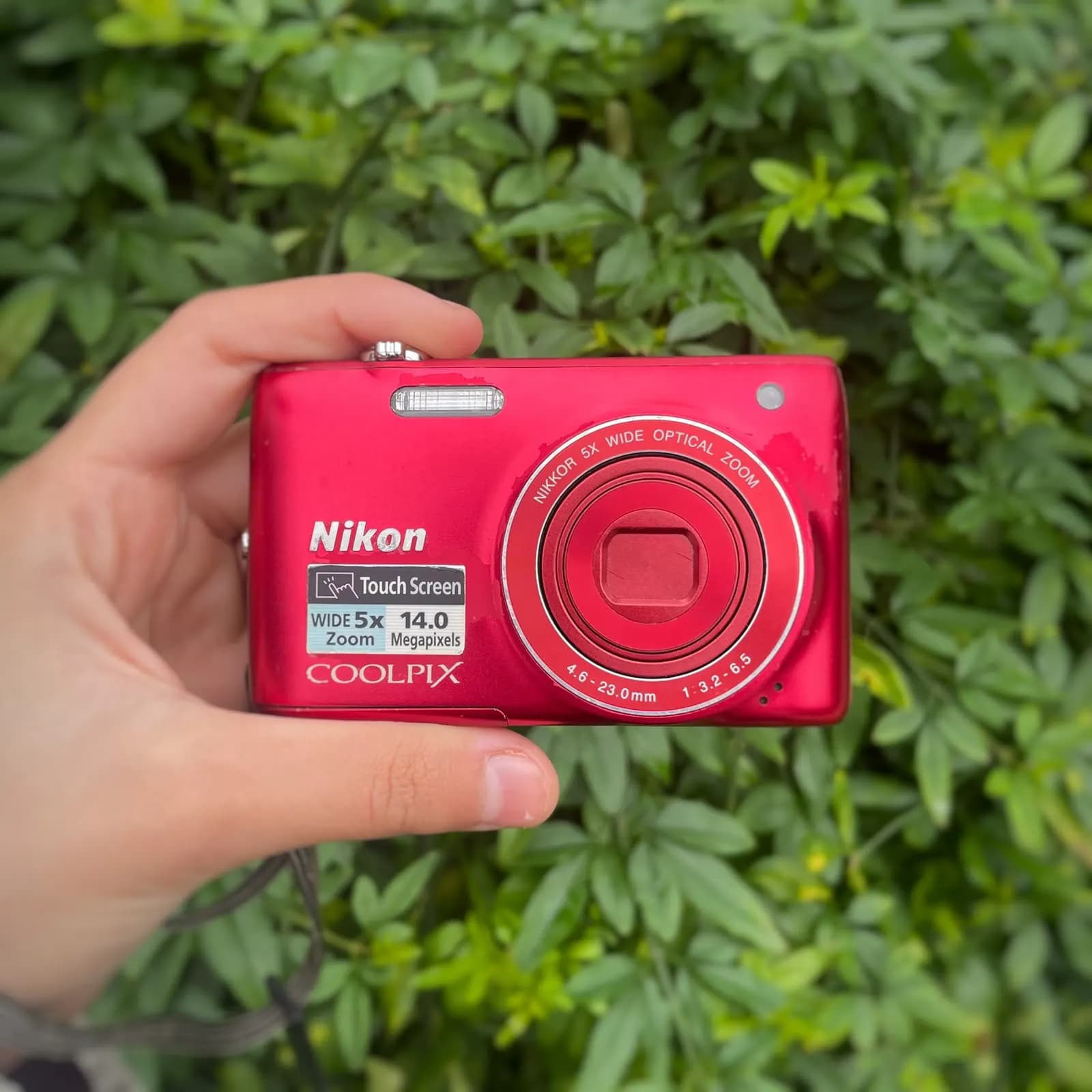 Cámara Nikon Coolpix roja con pantalla táctil sostenida en una mano, de frente